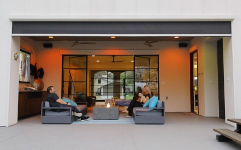 Two people sitting across from one another on an outdoor patio with a dog, watching TV